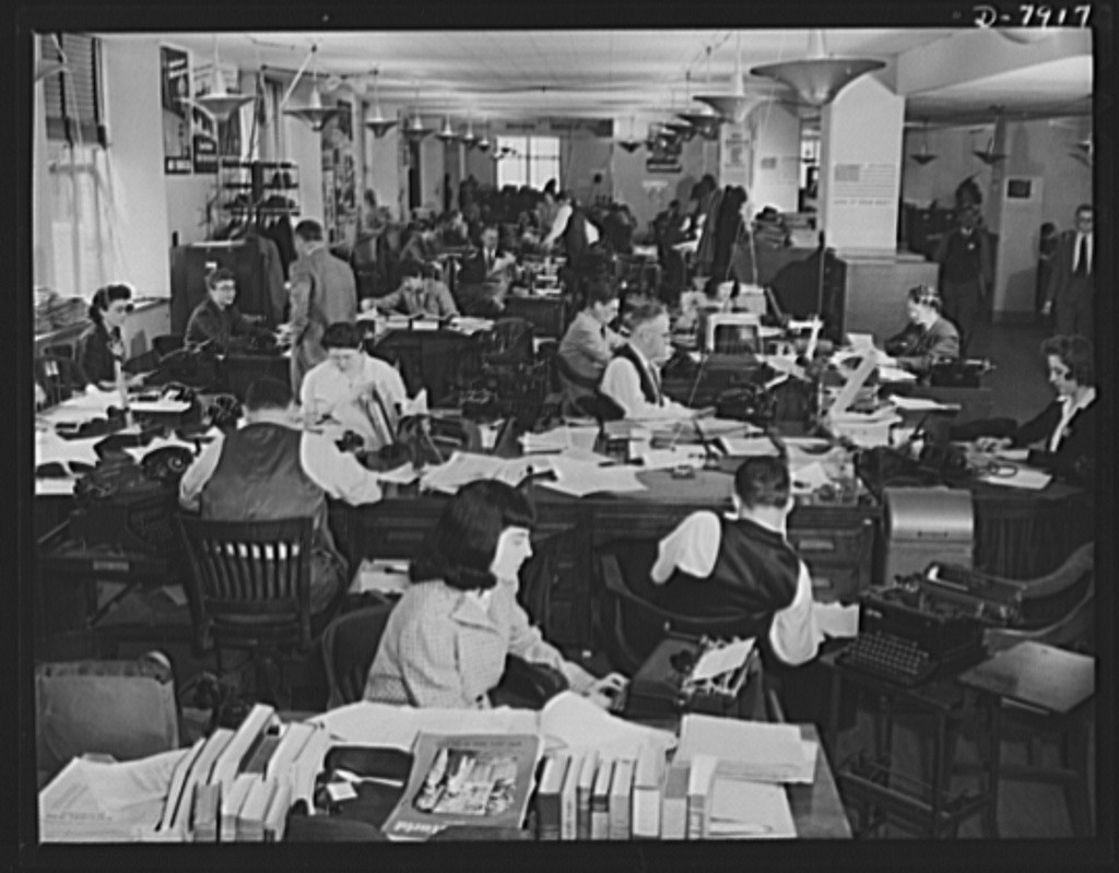 OWI Caption: "Office of War Information News Bureau. The News Bureau room of the OWI. It is arranged much the same way as the city room of a daily newspaper. Here, war news of the world is disseminated. In the foreground, are editors' desks handling such special services as trade press, women's activities, and campaigns. The news desk is in the background." Creator(s): Smith, Roger, photographer. Date Created/Published: 1942 Nov.