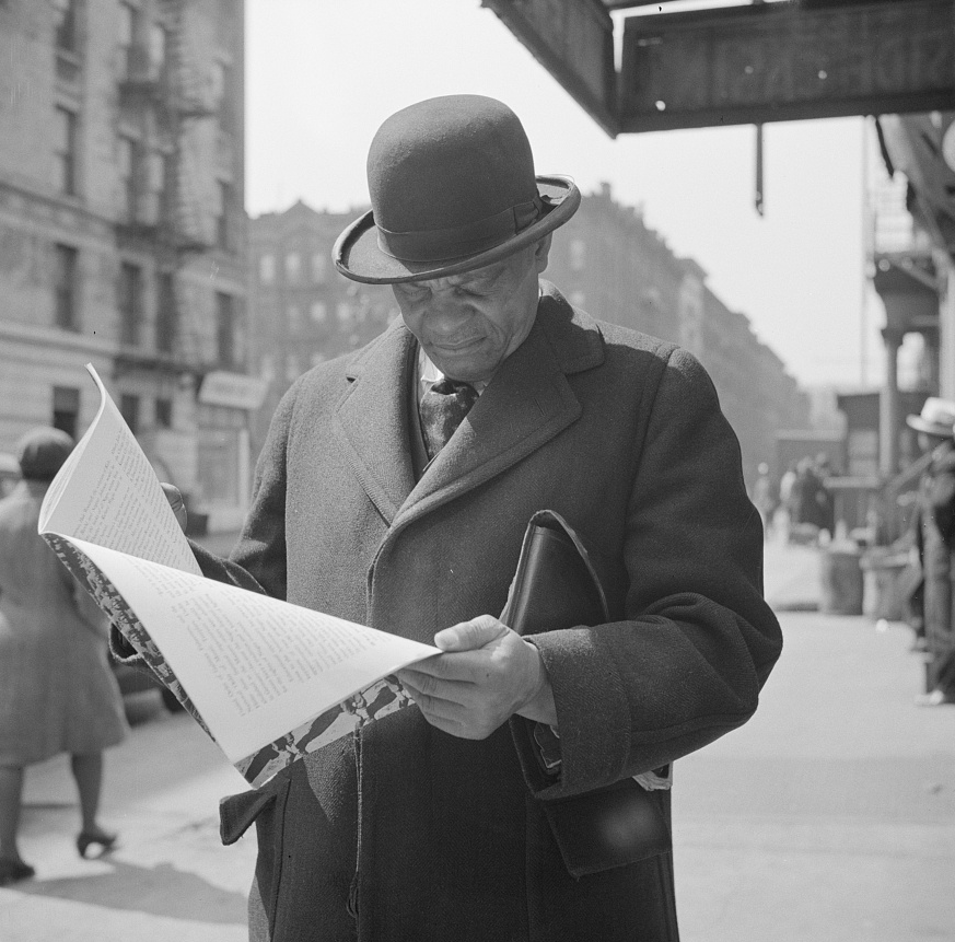 Photograph: New York, New York. A. Marcus Garveyite reading the OWI (Office of War Information) publication Negroes and the War, April 1943. Library of Congress Prints and Photographs Division, Washington, D.C. 20540, USA. OWI was the Executive Branch agency under the control of the White House. Its Overseas Division produced World War II shortwave radio broadcasts, which were later named the Voice of America (VOA).